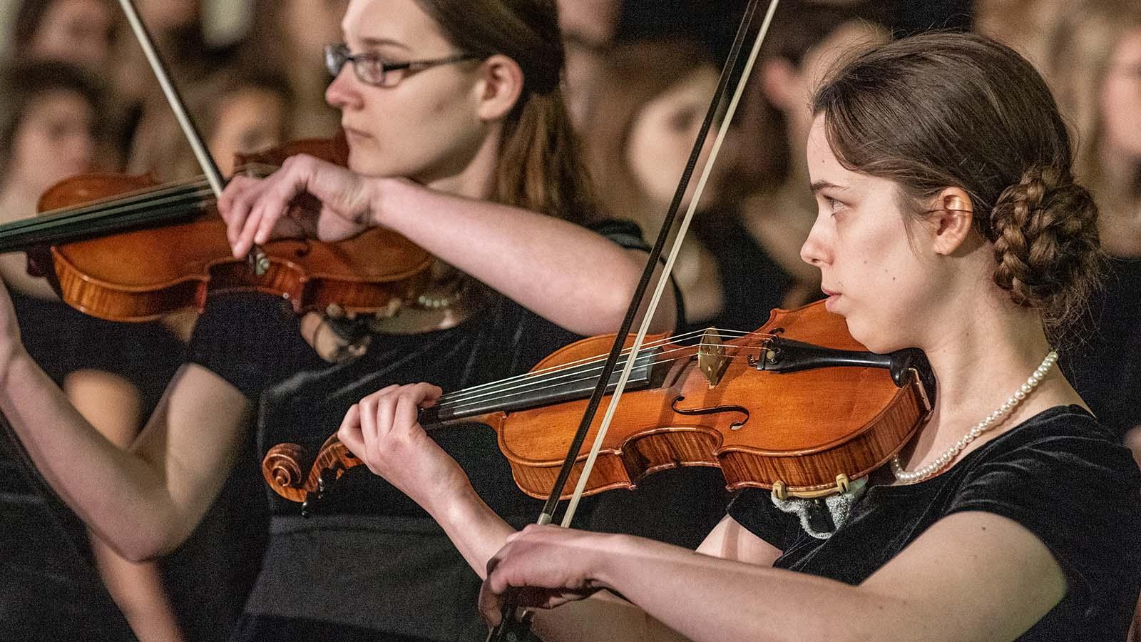 Two members of the string ensemble performing in front of choir